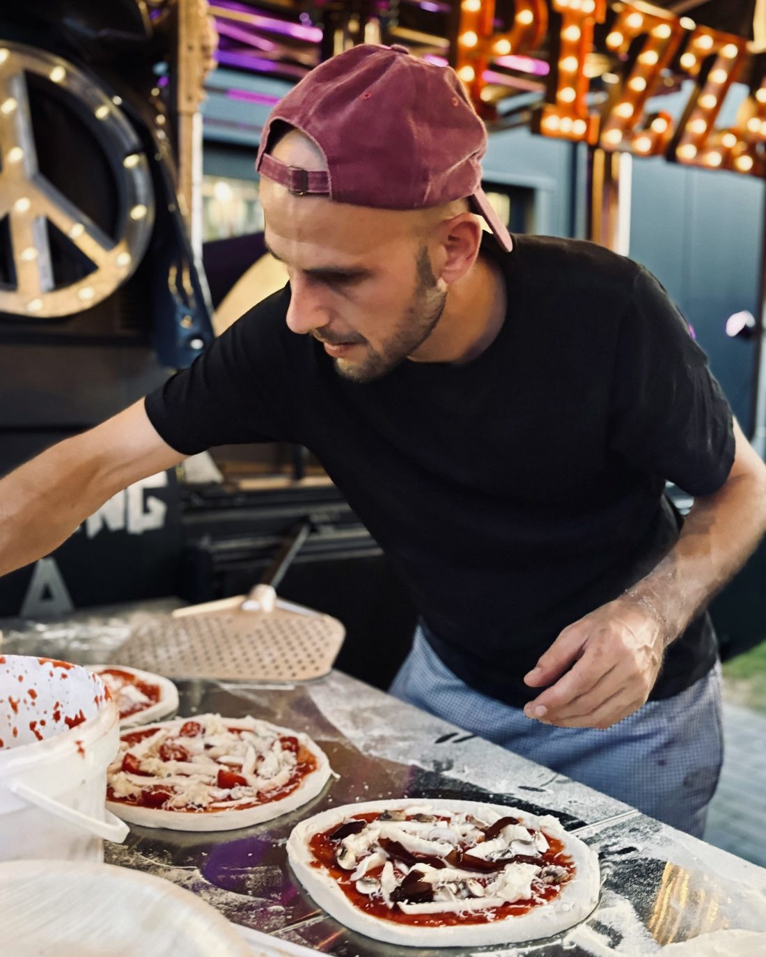 Gabor belegt Pizzen vor den leuchtenden Pizza-Buchstaben