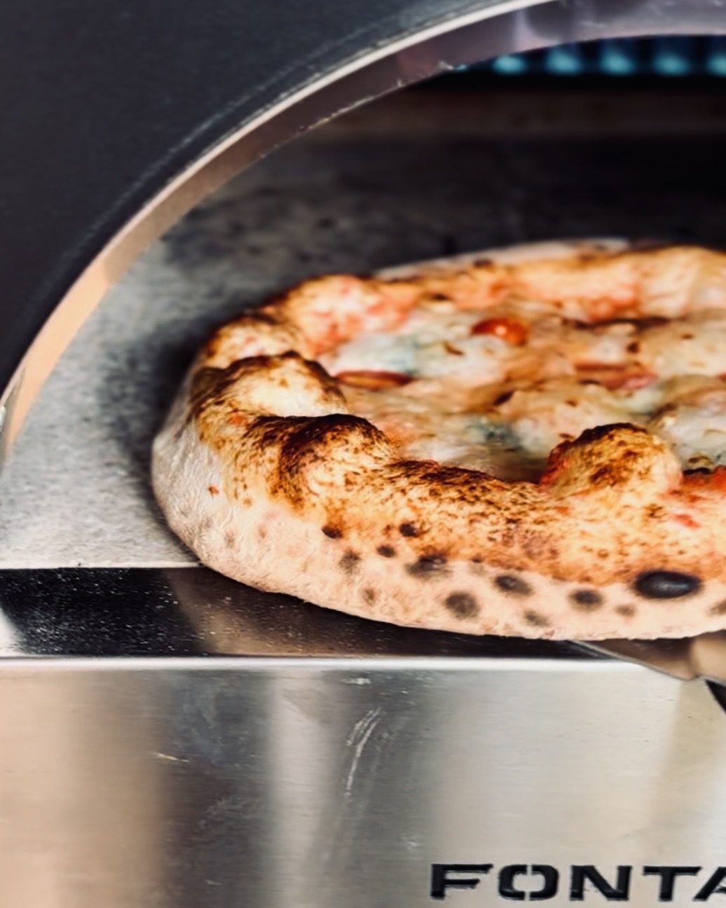 Fertige Pizza mit geleopardem Rand kommt aus dem Steinofen