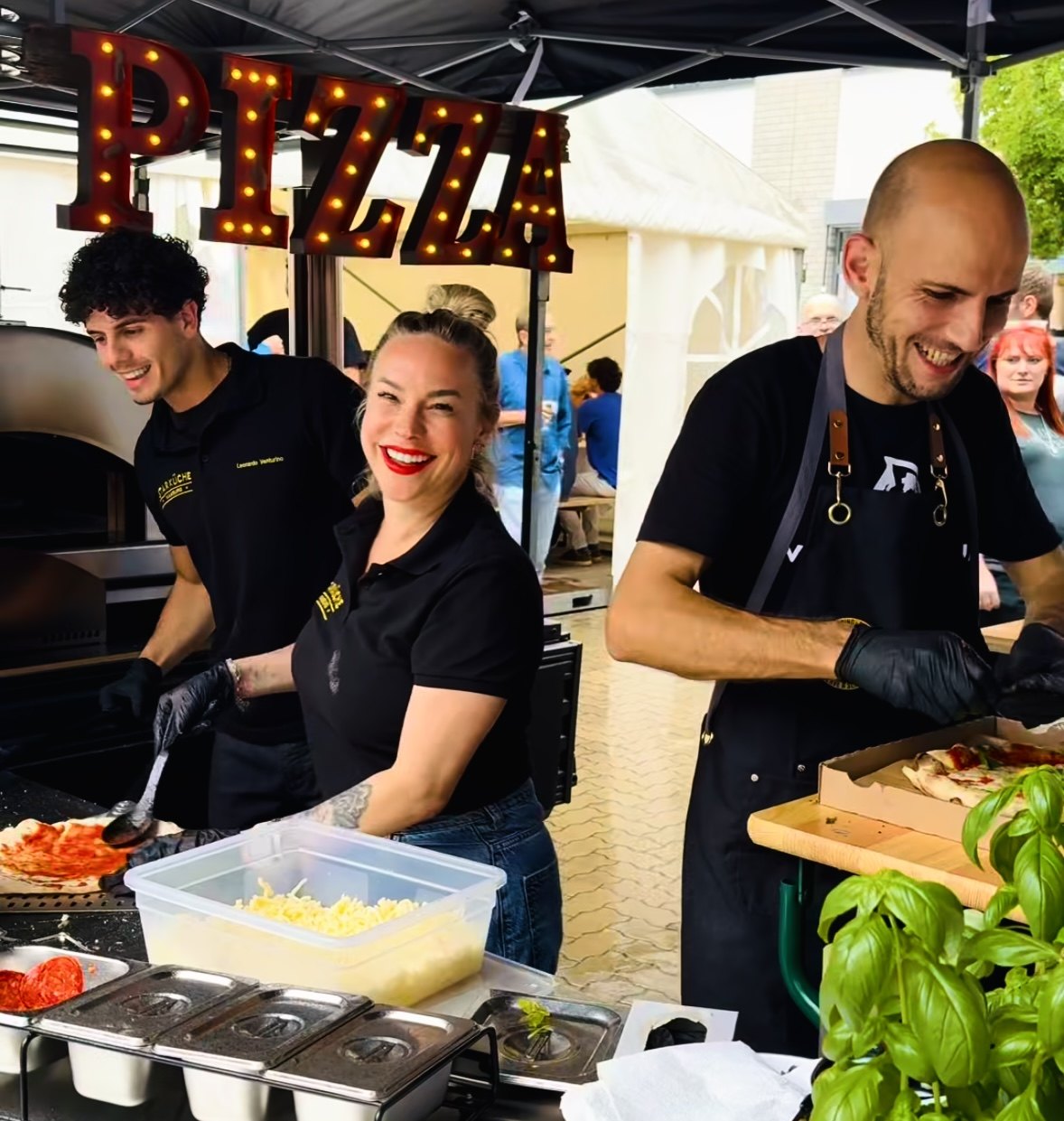 Das Team am Pizzastand unter den leuchtenden Pizza-Buchstaben